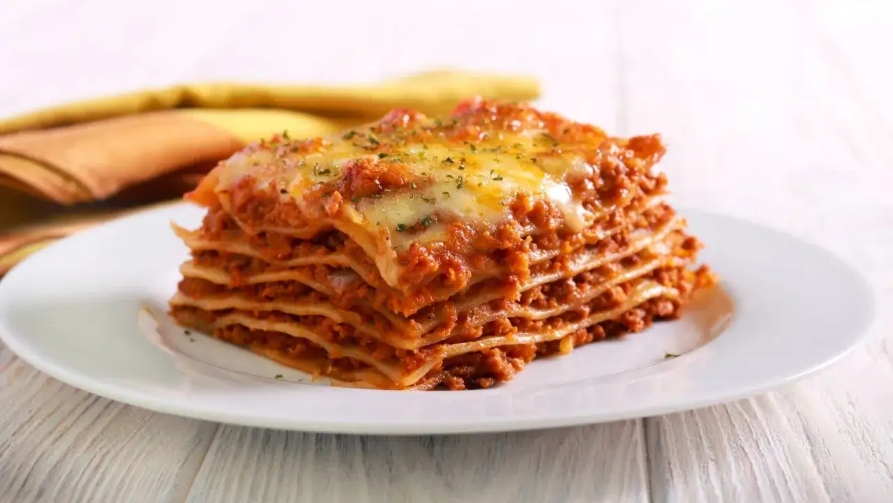 Una porci&oacute;n generosa de lasa&ntilde;a de carne, con capas de pasta, salsa bolo&ntilde;esa y queso derretido, servida en un plato blanco.