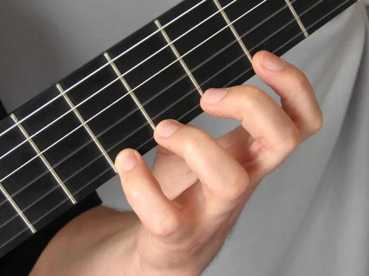 Dłoń z palcami dociskającymi struny gitary elektrycznej. Pokazano prawidłowy sposób, jak trzymać gitarę elektryczną, ćwicząc akord.