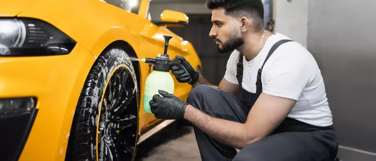 Mann mit Handschuhen sprüht gelbe Flüssigkeit auf ein gelbes Auto. Ein einfacher felgenreiniger hausmittel für glänzende Felgen.