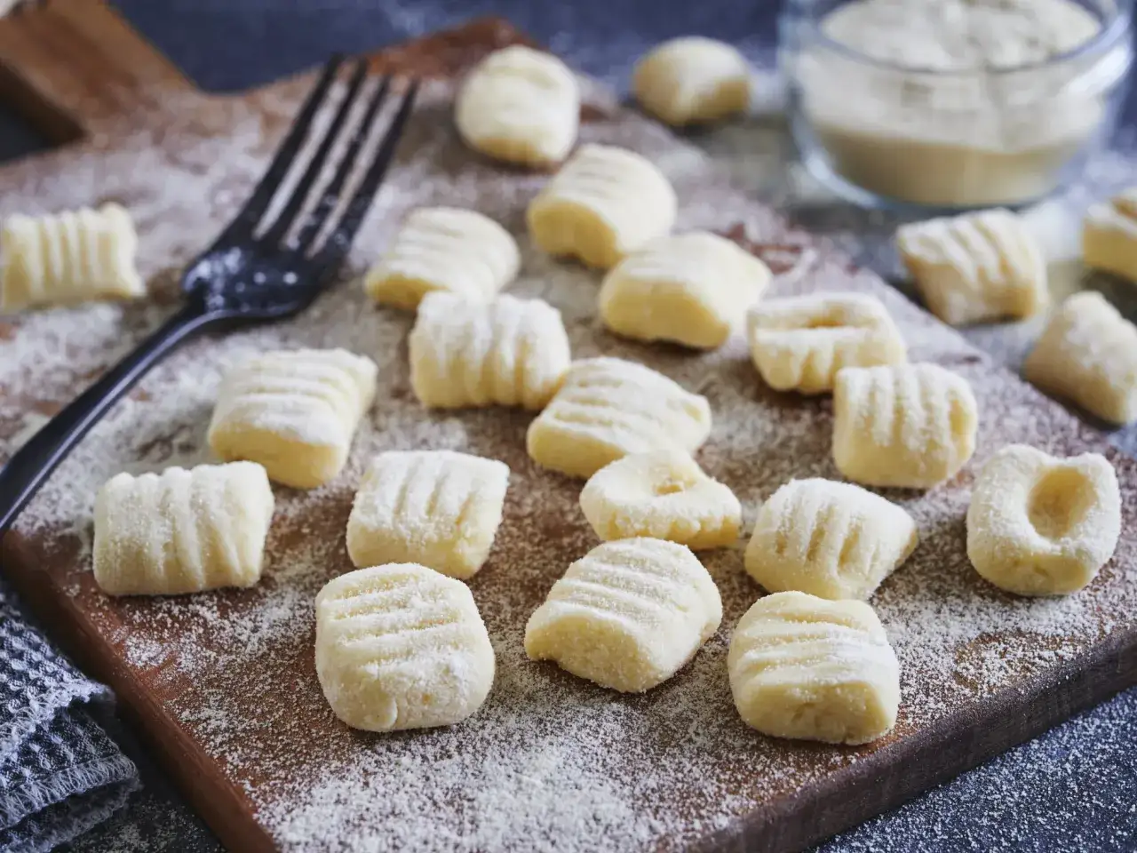 Frische Gnocchi, bereit f&uuml;r italienische Rezepte, liegen auf einem Holzbrett, best&auml;ubt mit Mehl. Eine Gabel liegt daneben.