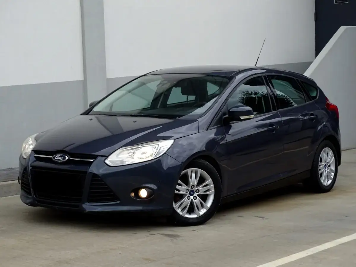 Ciemnogranatowy Ford Focus MK3 1.6 TDCI, hatchback, zaparkowany na betonowym placu przed budynkiem.