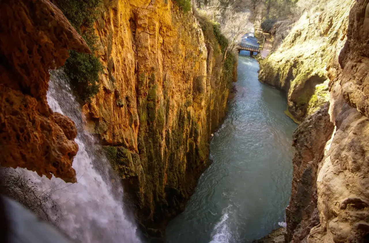 Cascada y r&iacute;o en un ca&ntilde;&oacute;n, ideal para excursiones cerca de Zaragoza con agua. Un puente de madera cruza el r&iacute;o.