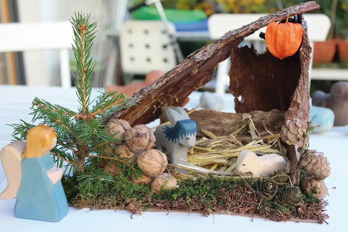 Eine einfache Krippe basteln Kinder mit Holzfiguren, Tannenzweigen, N&uuml;ssen und Rinde. Ein s&uuml;&szlig;er Esel und ein Lamm sind zu sehen.