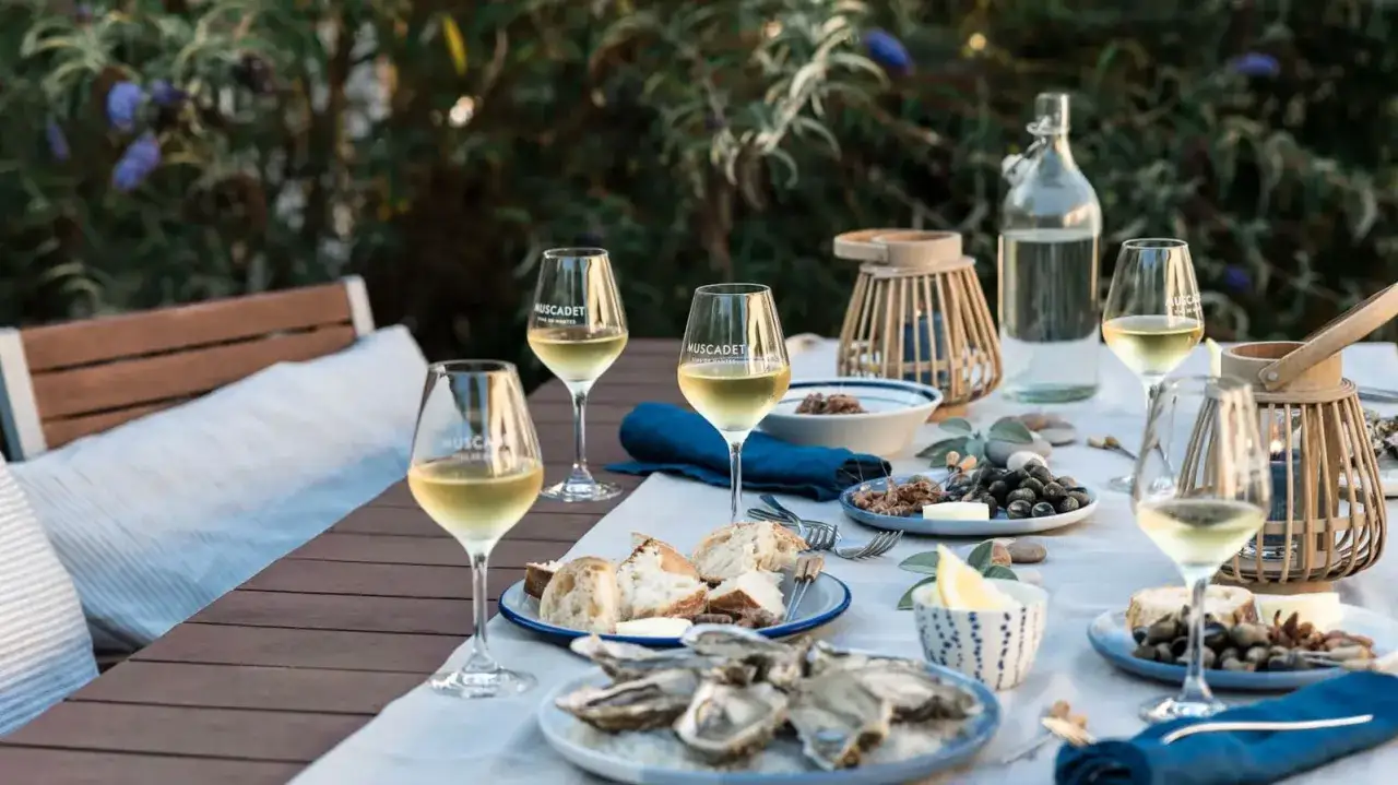 Ein gedeckter Tisch mit Austern, Brot und Gläsern voller Muscadet, einem Wein aus der Melon de Bourgogne Traube, lädt zum Genuss ein.