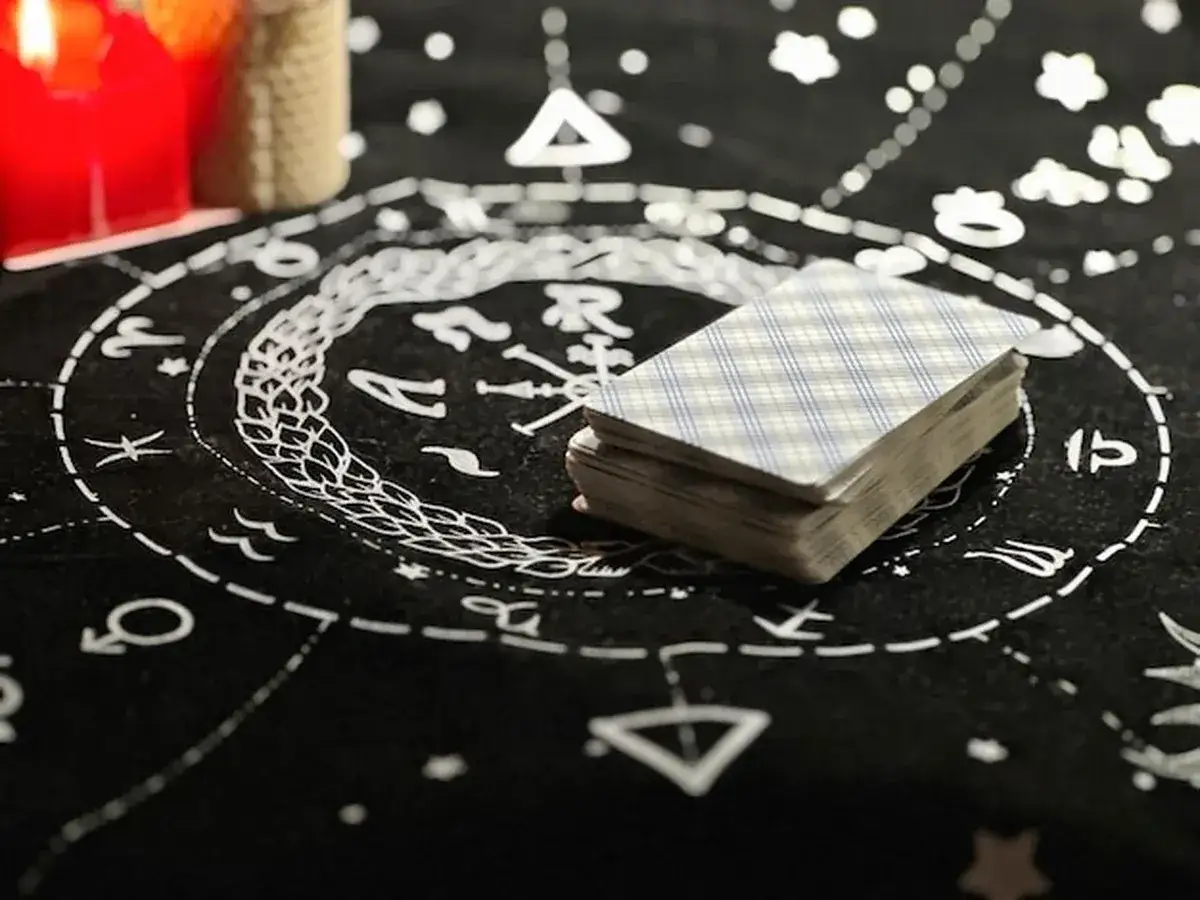 Talia kart tarota na czarnym obrusie z symbolami zodiaku. Czerwona świeca i inne przedmioty tworzą mistyczną atmosferę, sugerując głębokie 000 znaczenie.