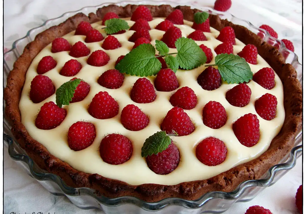 Pyszna tarta z mascarpone i białą czekoladą, ozdobiona malinami i listkami mięty. Idealna na deser.