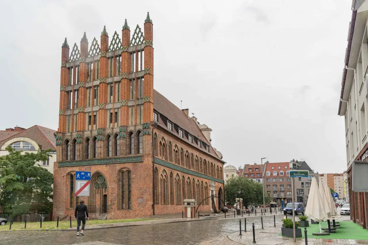 Ein Mann geht durch die regennasse **Stettin Altstadt** an einem Backsteingebäude mit Spitzdächern vorbei.