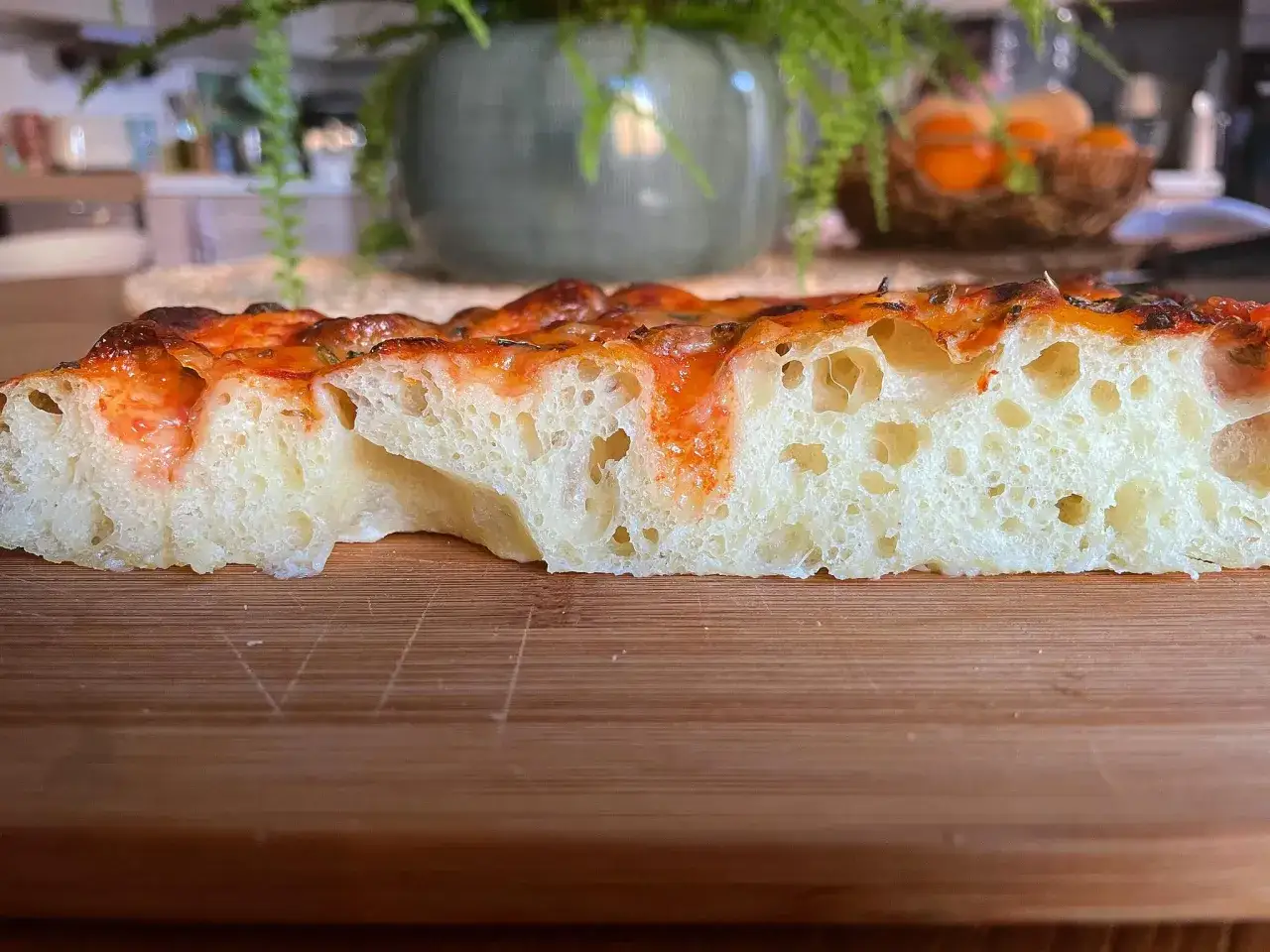 Fetta di focaccia soffice e alveolata, con pomodoro e formaggio filante. Perfetta per uno spuntino o un pasto veloce.