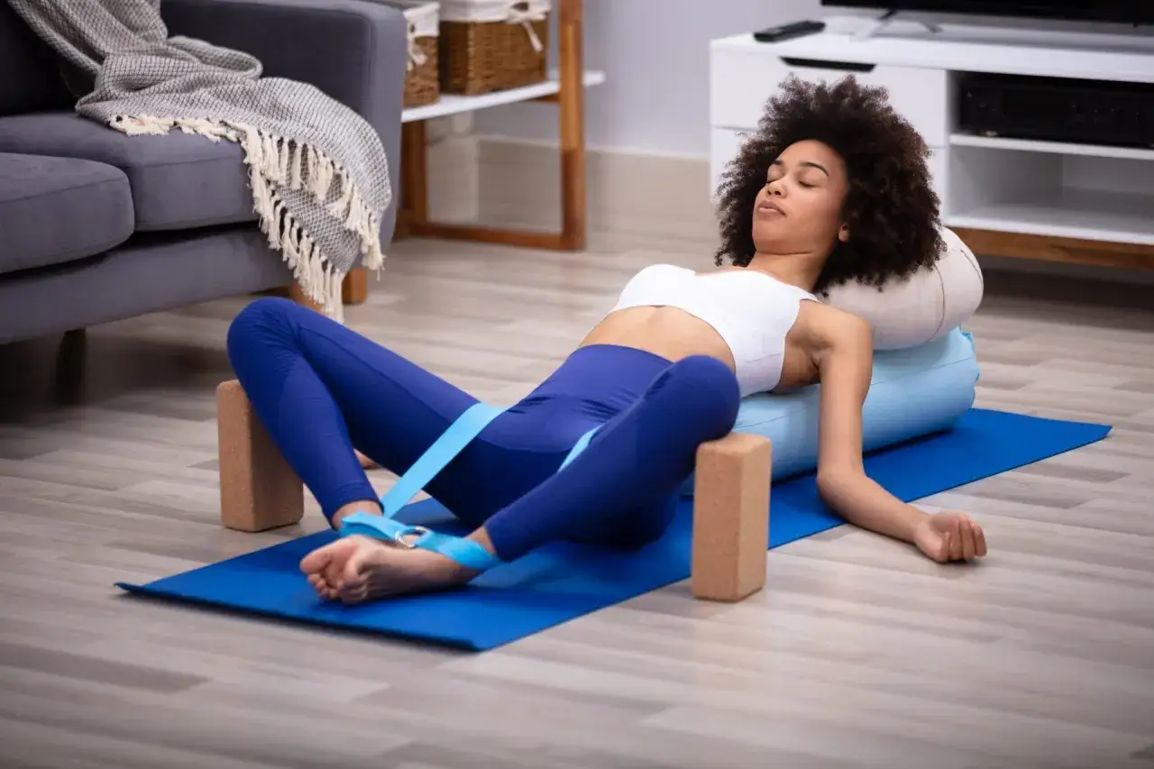 Frau entspannt sich in einer Yoga-Pose mit Kissen und Bl&ouml;cken. Ein guter Weg, um mit Yoga anzufangen und Stress abzubauen.