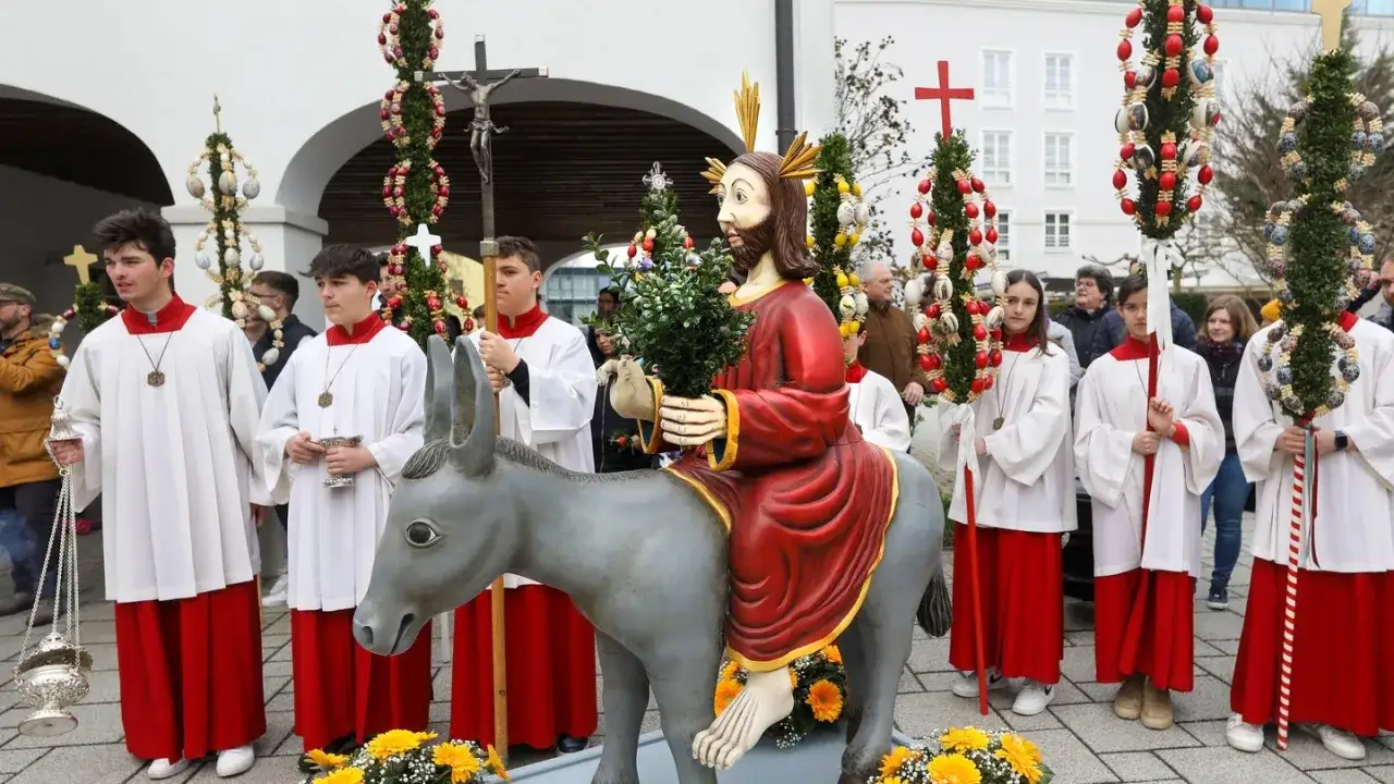 Feierlicher Umzug zum gesegneten Palmsonntag mit Jesusfigur auf einem Esel, Ministranten und geschm&uuml;ckten Palmst&ouml;cken.