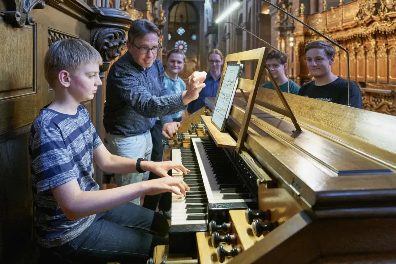 Jugendlicher &uuml;bt an einer Kirchenorgel, w&auml;hrend ein Lehrer Anweisungen gibt. Vielleicht eine Anzeige f&uuml;r kirchenmusik stellenangebote?