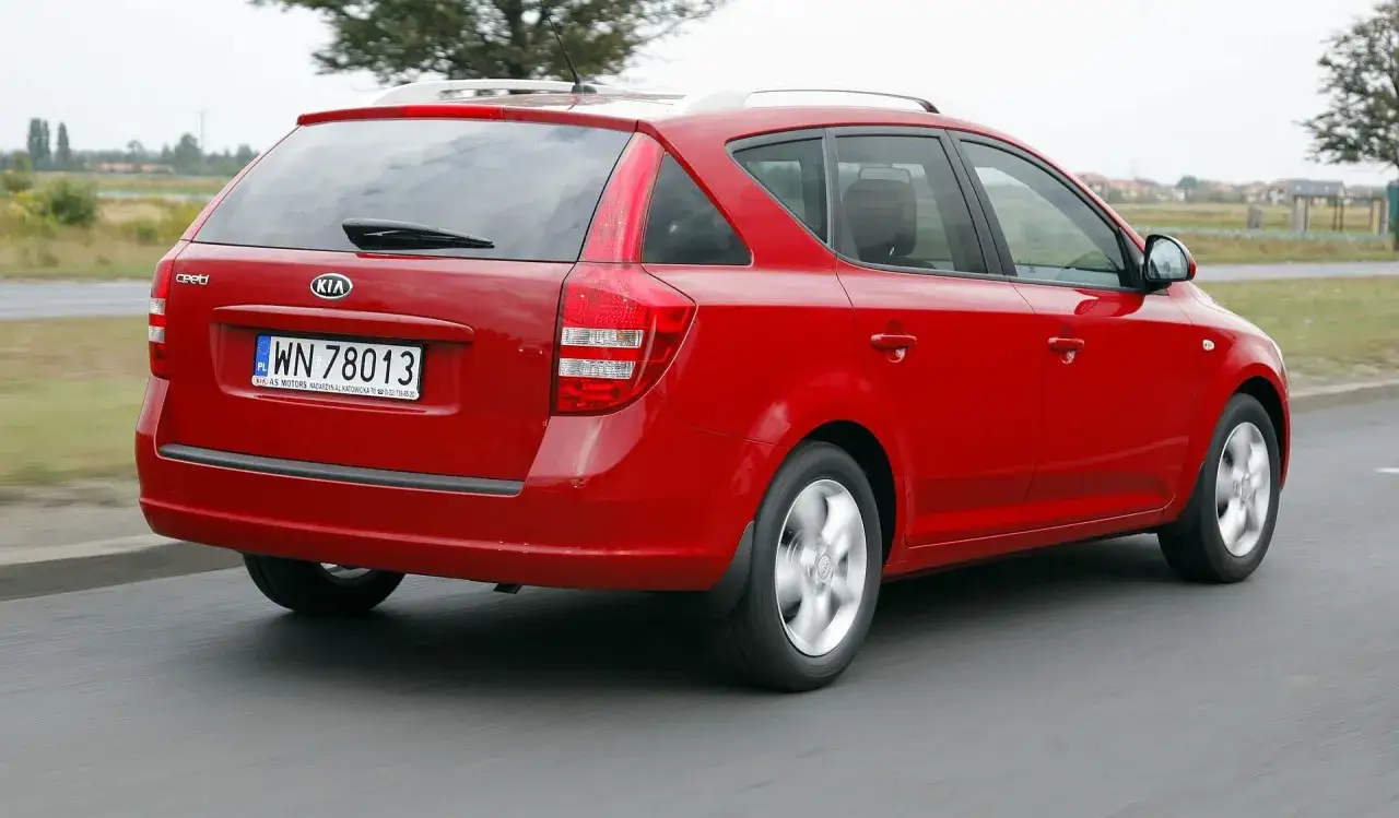 Czerwony Kia Ceed kombi 2009 na drodze, z widocznym bagażnikiem i tylnymi światłami.