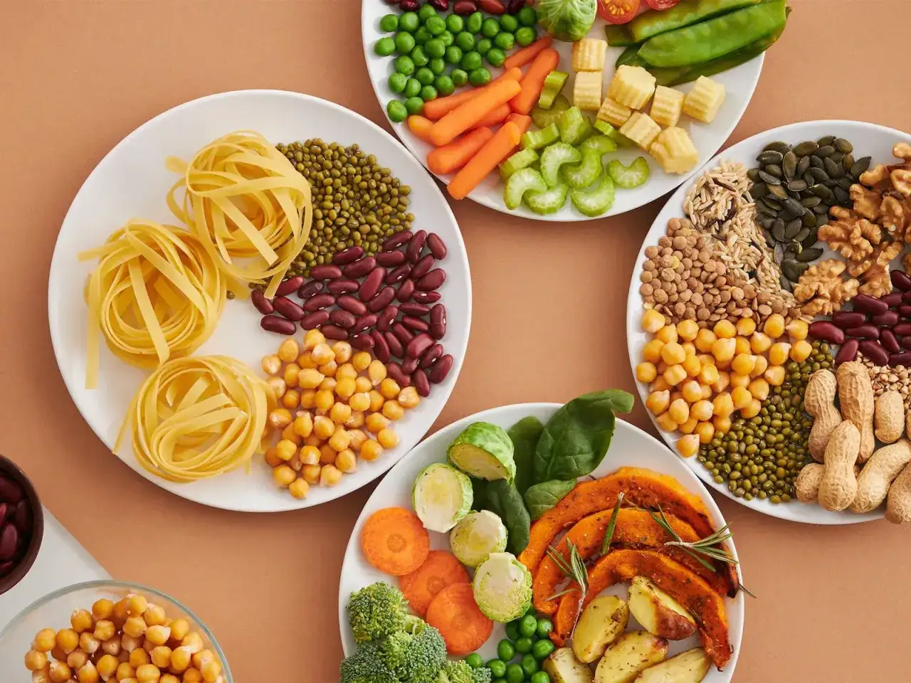 Platos llenos de alimentos con mucha fibra: pasta, frijoles, garbanzos, lentejas, nueces, semillas, brócoli, zanahorias, calabaza y más.