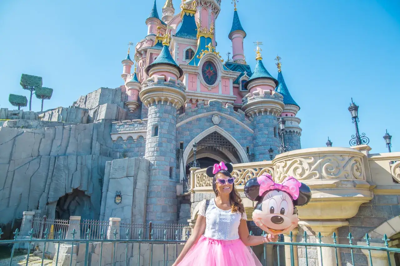 Uśmiechnięta dziewczyna z balonem Myszki Miki przed zamkiem. Zastanawiasz się, ile kosztuje Disneyland?