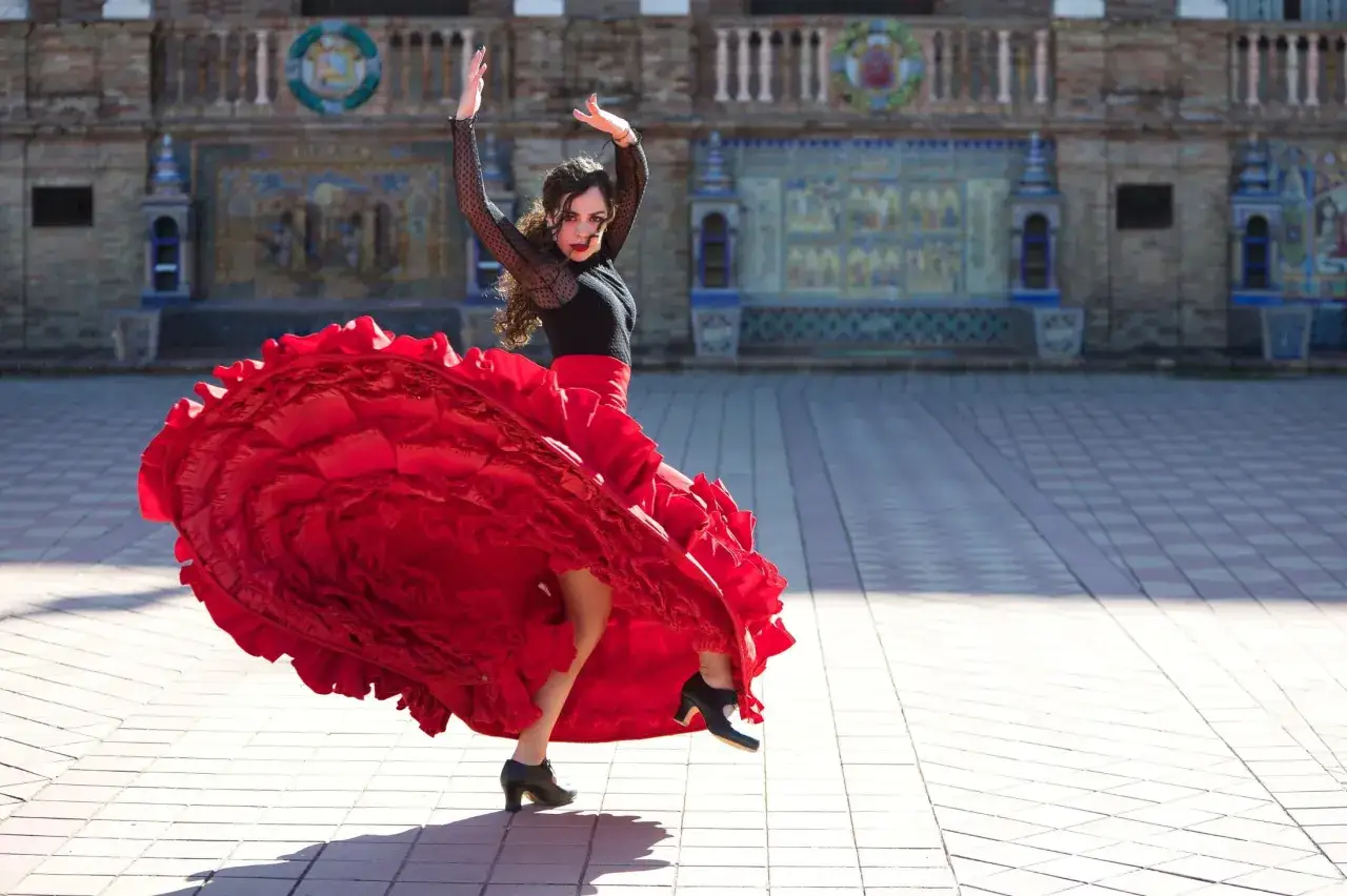 Tancerka flamenco w zwiewnej, czerwonej sukni wiruje na tle zabytkowej architektury.