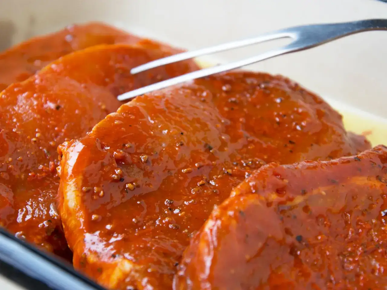 Zartes **Schweinefleisch marinieren** in einer w&uuml;rzigen Sauce. Eine Gabel liegt bereit, um die saftigen St&uuml;cke zu wenden.