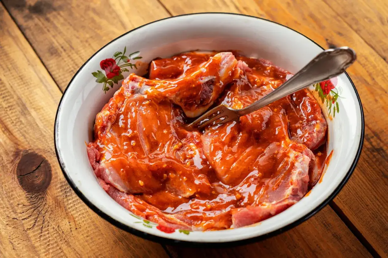Morceaux de bœuf dans une marinade orangée, prêts à être cuits. Une fourchette est plantée dans la viande.