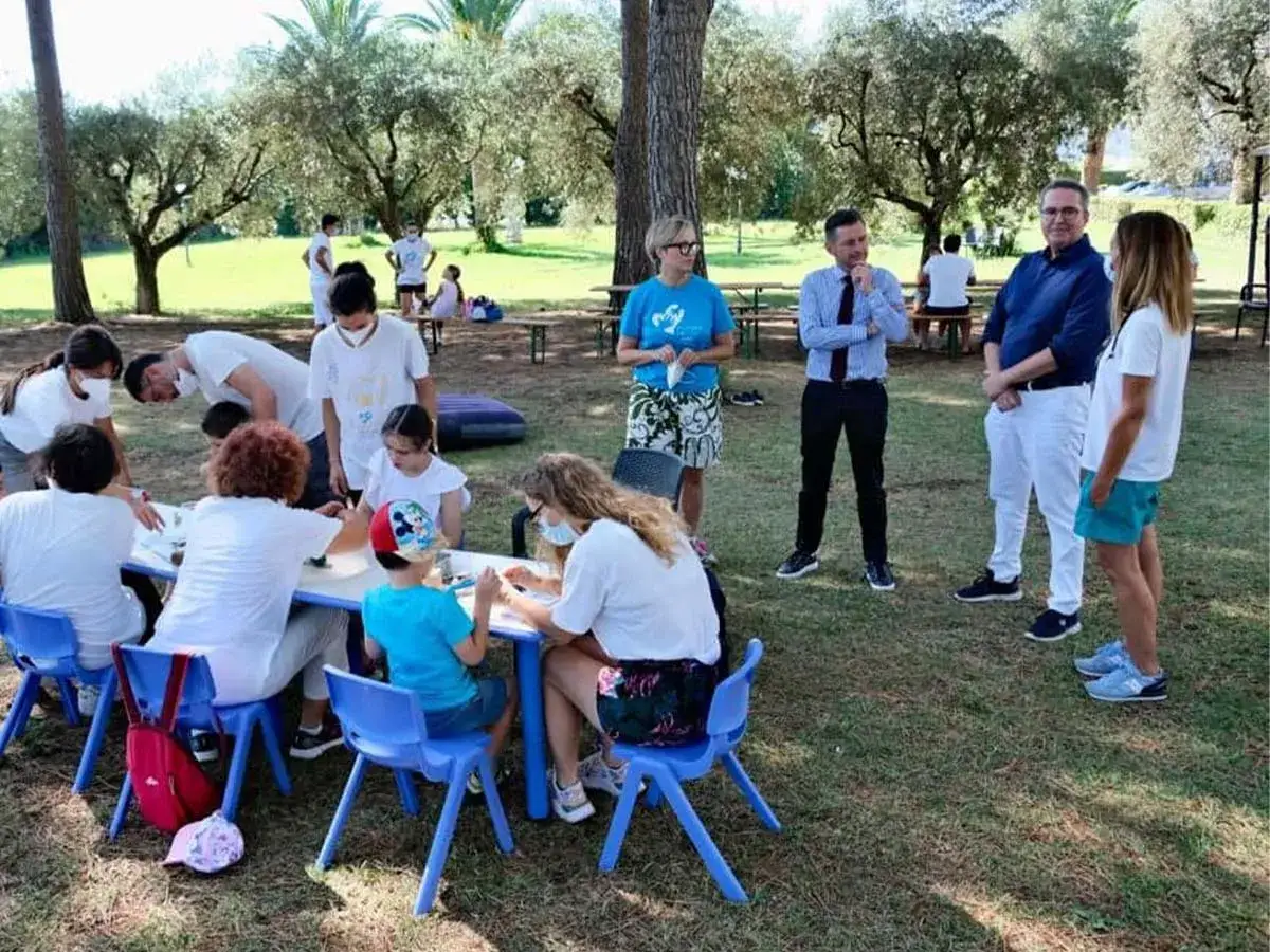 Bambini e adulti partecipano ad attività all'aperto, forse legate all'indennità di frequenza mesi estivi.