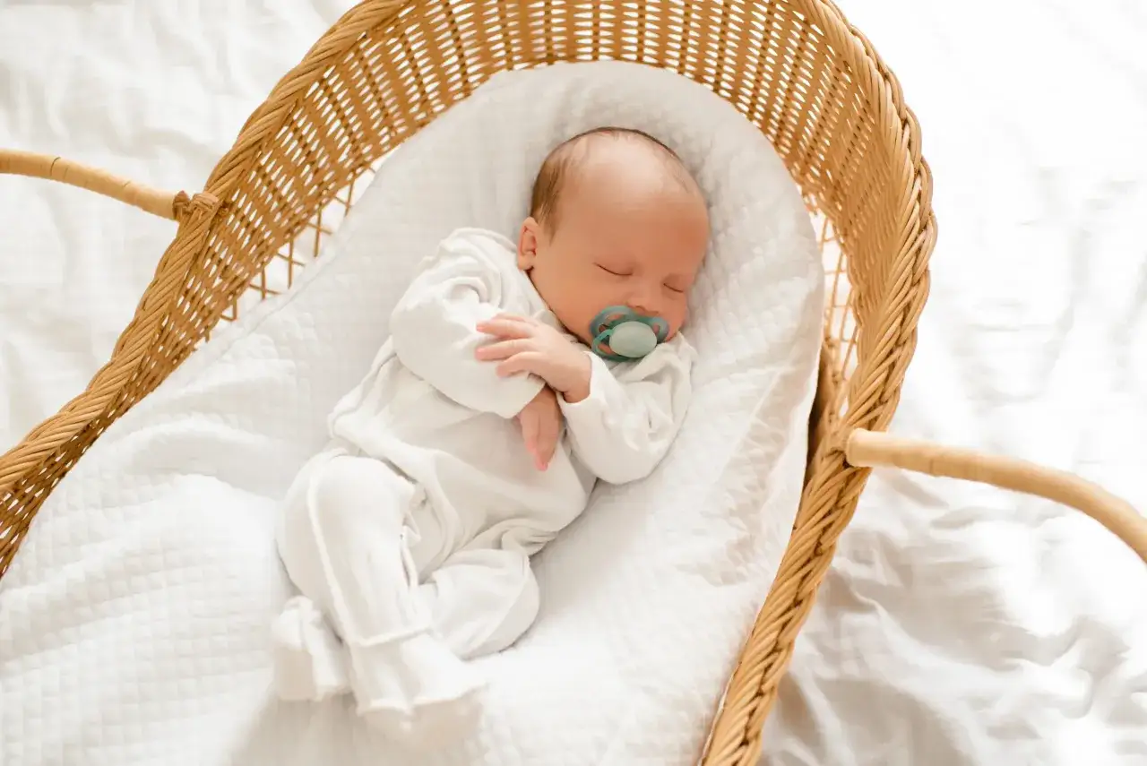 Un bebé duerme plácidamente en una cesta de mimbre, con un chupete en la boca. La tabla sueño bebe es perfecta para sus dulces sueños.