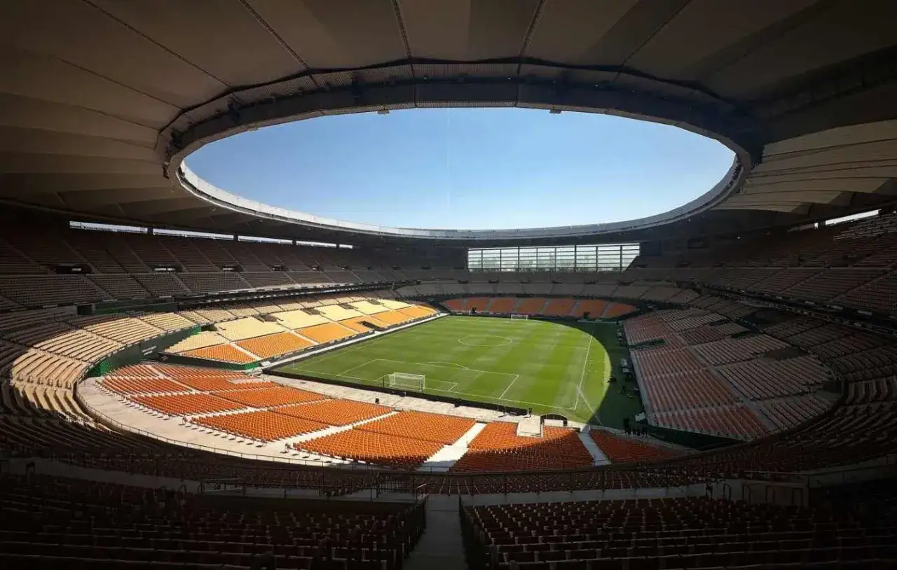 Puste trybuny stadionu Estadio de la Cartuja czekają na kibiców. Zielona murawa boiska lśni w słońcu.