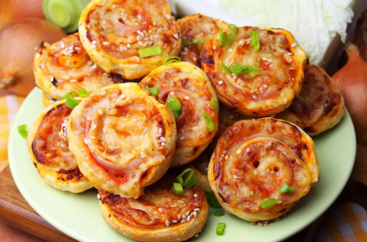 Pizzerinki z ciasta francuskiego, posypane sezamem i szczypiorkiem, wyglądają apetycznie. Idealne na szybką przekąskę.