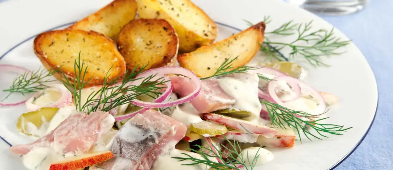 Ein Teller mit Matjes, Kartoffelspalten, Zwiebelringen und Dill. Ein köstlicher Matjes-Salat mit frischen Zutaten.
