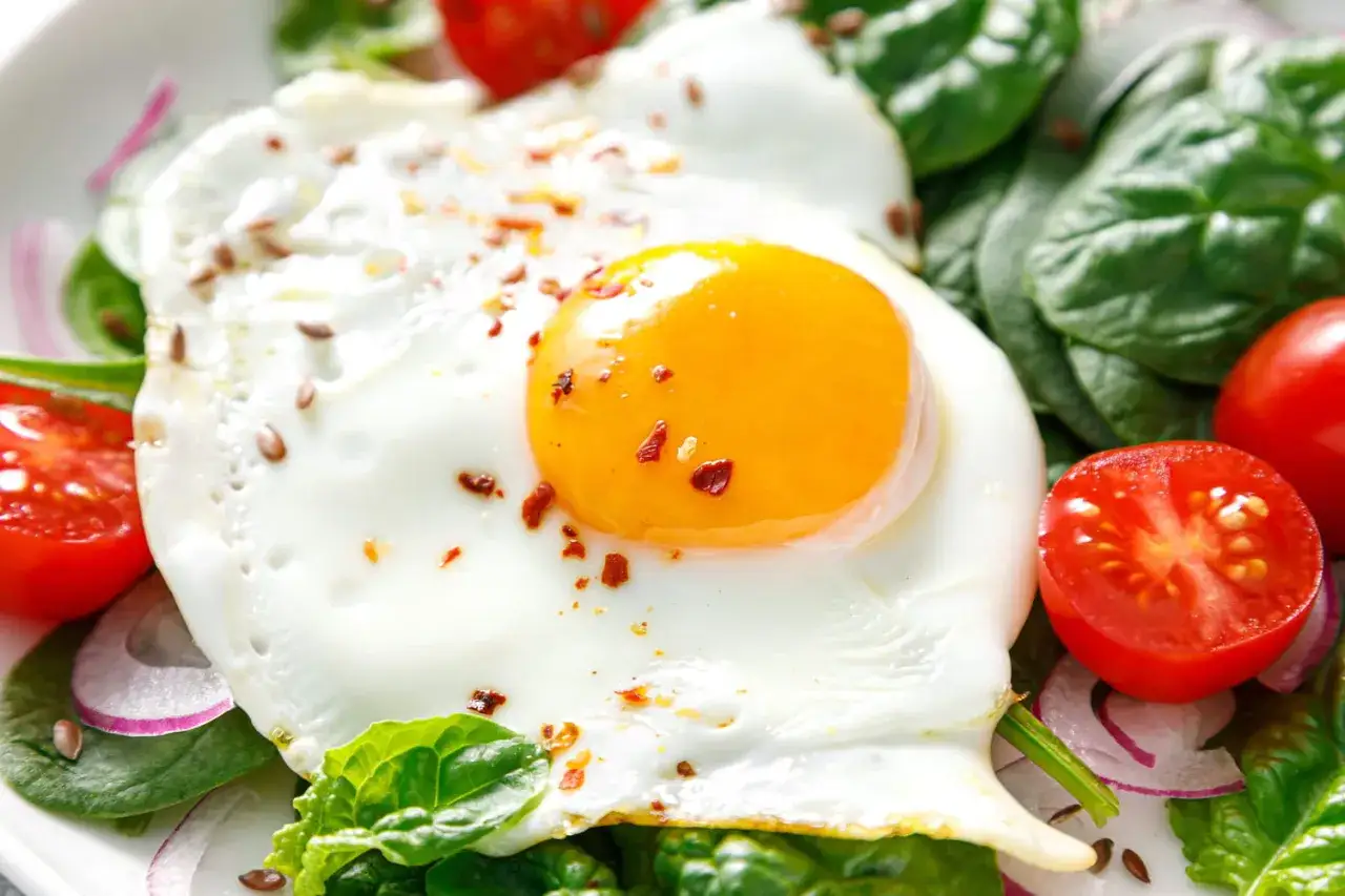 Un œuf sur le plat, parsemé de graines de lin et de flocons de piment, repose sur un lit d'épinards frais, de tomates cerises et d'oignons rouges.