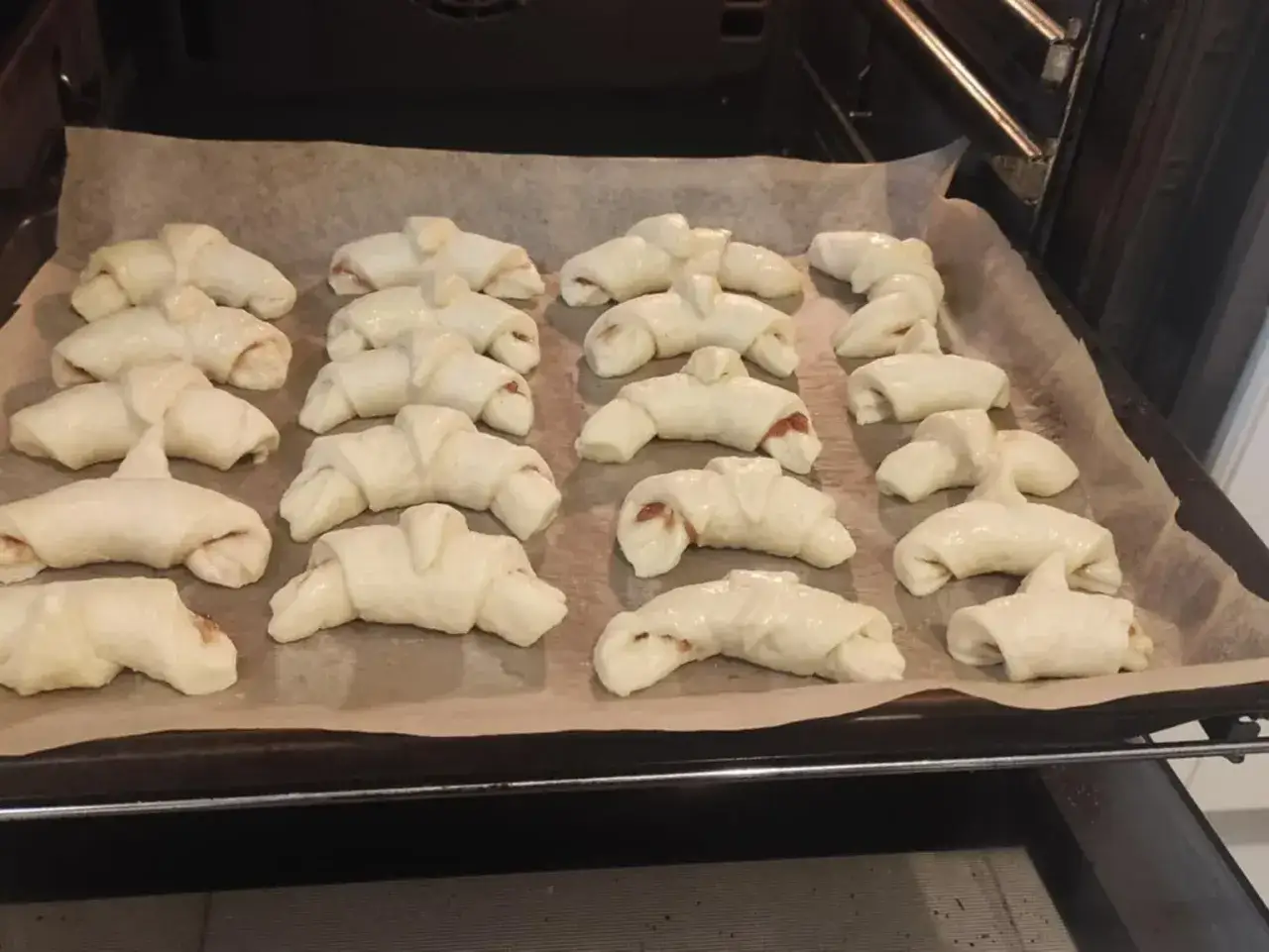 Gotowe do pieczenia rogaliki z marmoladą, ułożone na blasze wyłożonej papierem.