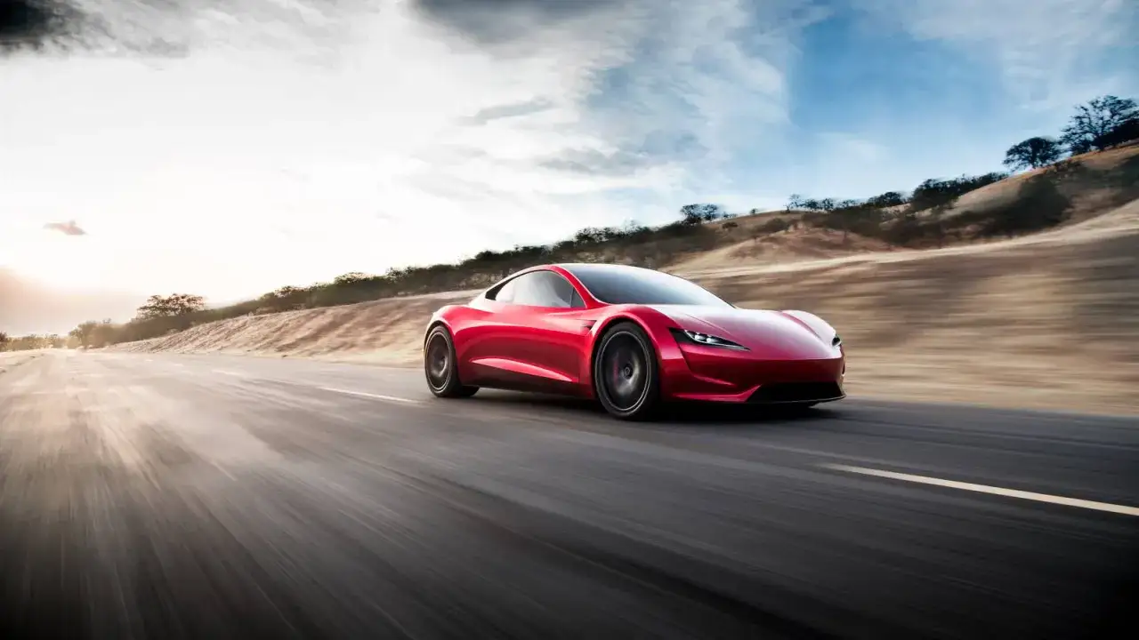 Czerwony Tesla Roadster pędzi po pustej drodze, krajobraz rozmyty przez prędkość.