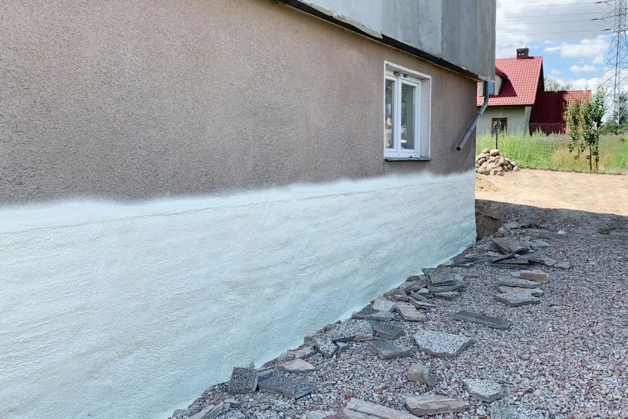 Ocieplenie murłaty pianką poliuretanową zabezpiecza fundamenty przed utratą ciepła. Widoczny fragment ściany budynku z nałożoną izolacją.