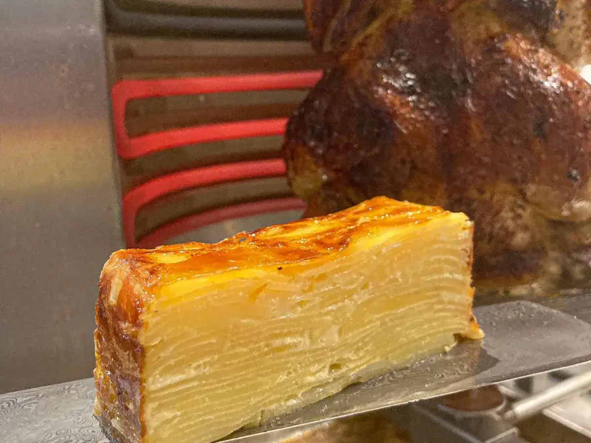 En perfekt skiva pommes anna, gyllene och krispig, bredvid en helrostad kyckling.