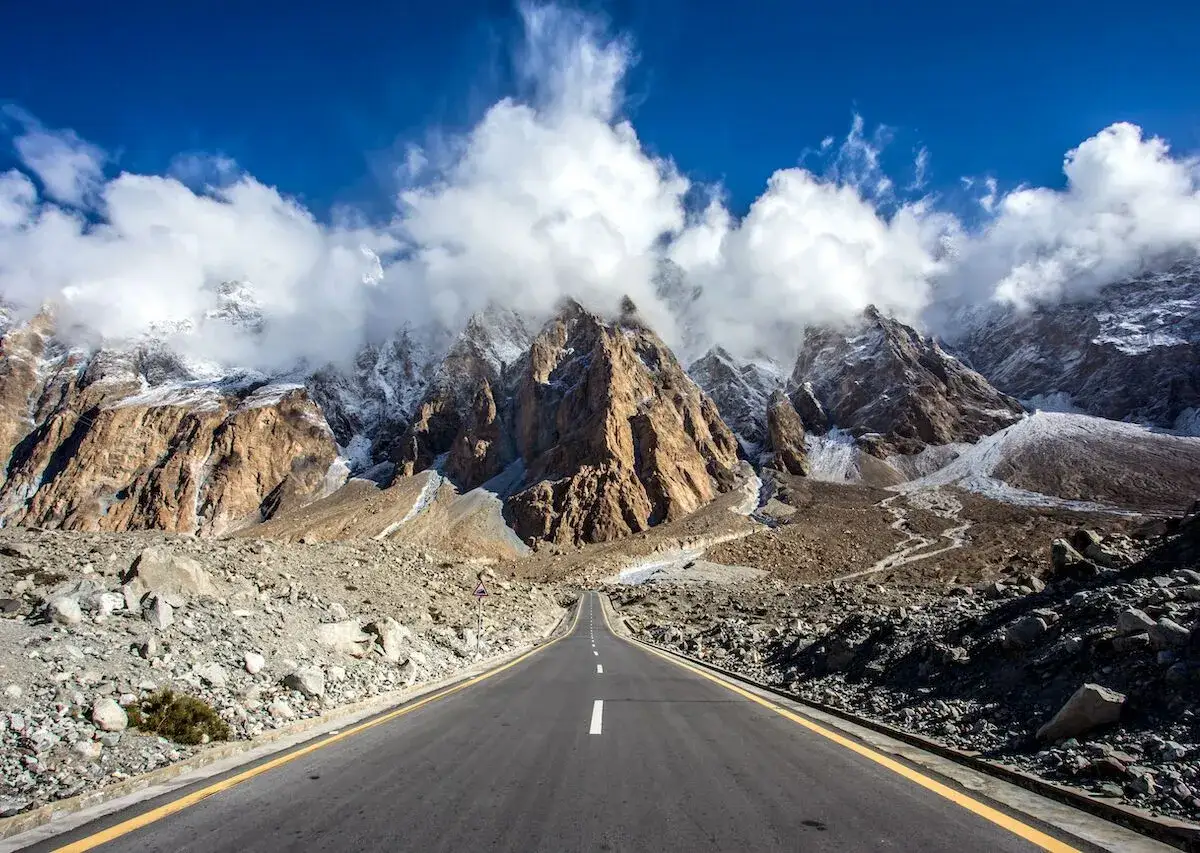 Droga w Karakoram Highway prowadzi przez surowe, skaliste góry z ośnieżonymi szczytami i chmurami.