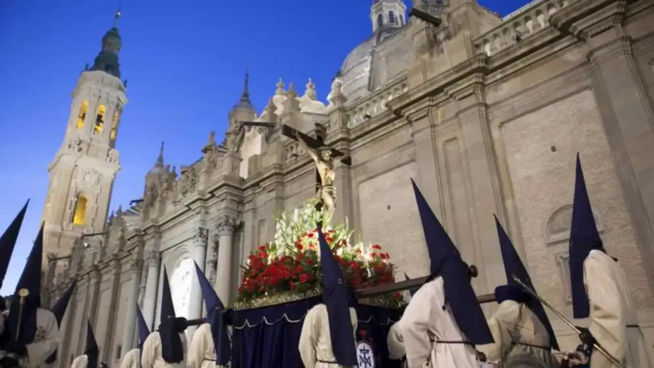 Procesión de Semana Santa en Zaragoza, con nazarenos y un paso de Cristo frente a la Basílica del Pilar. Una imagen de la ruta cofrade.