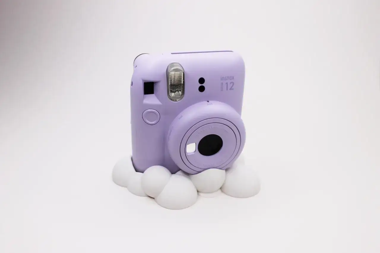 Fioletowy aparat Instax Mini 12 na białym tle, gotowy do robienia zdjęć.