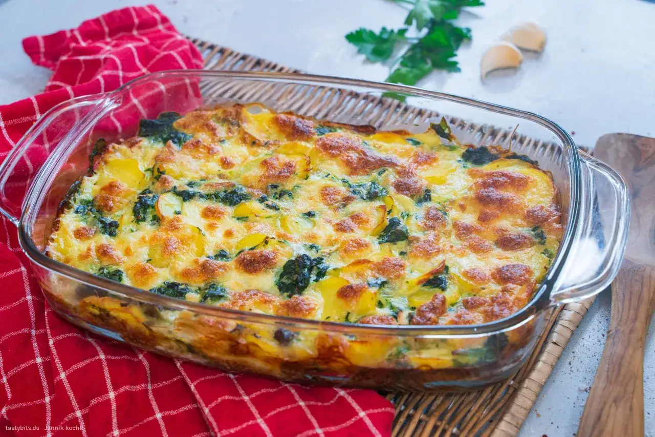 Goldbraun überbackener Kartoffel-Spinat-Auflauf in einer Glasform, garniert mit Petersilie und Knoblauch.