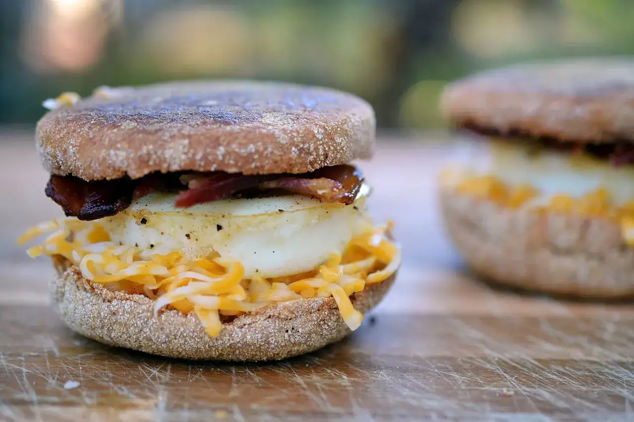 Pyszny mcmuffin farmerski z jajkiem sadzonym, chrupiącym boczkiem i startym serem. Idealny na śniadanie.