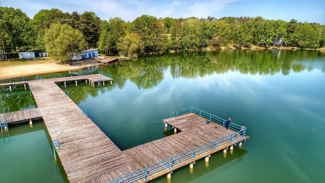 Drewniane pomosty nad spokojnymi jeziora zielona góra, otoczone zielenią. Dwa wędkarze łowią ryby.