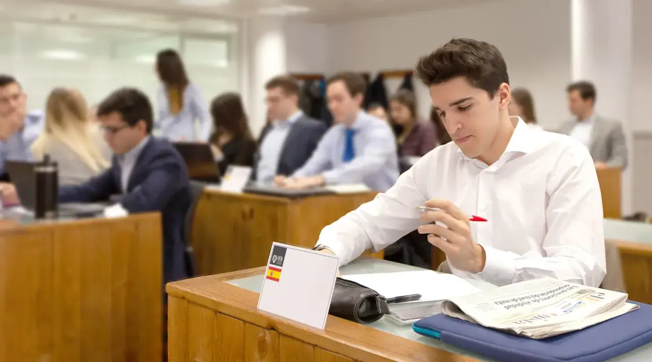 Estudiantes en un aula, uno concentrado en sus apuntes. El master MBA precio es una inversi&oacute;n en tu futuro.
