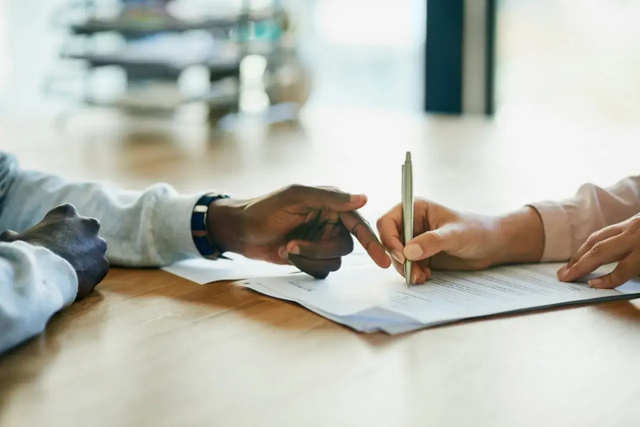 Main tenant signe un document, son doigt pointant vers une clause. Il ne veut pas renouveler son CDD fonction publique.