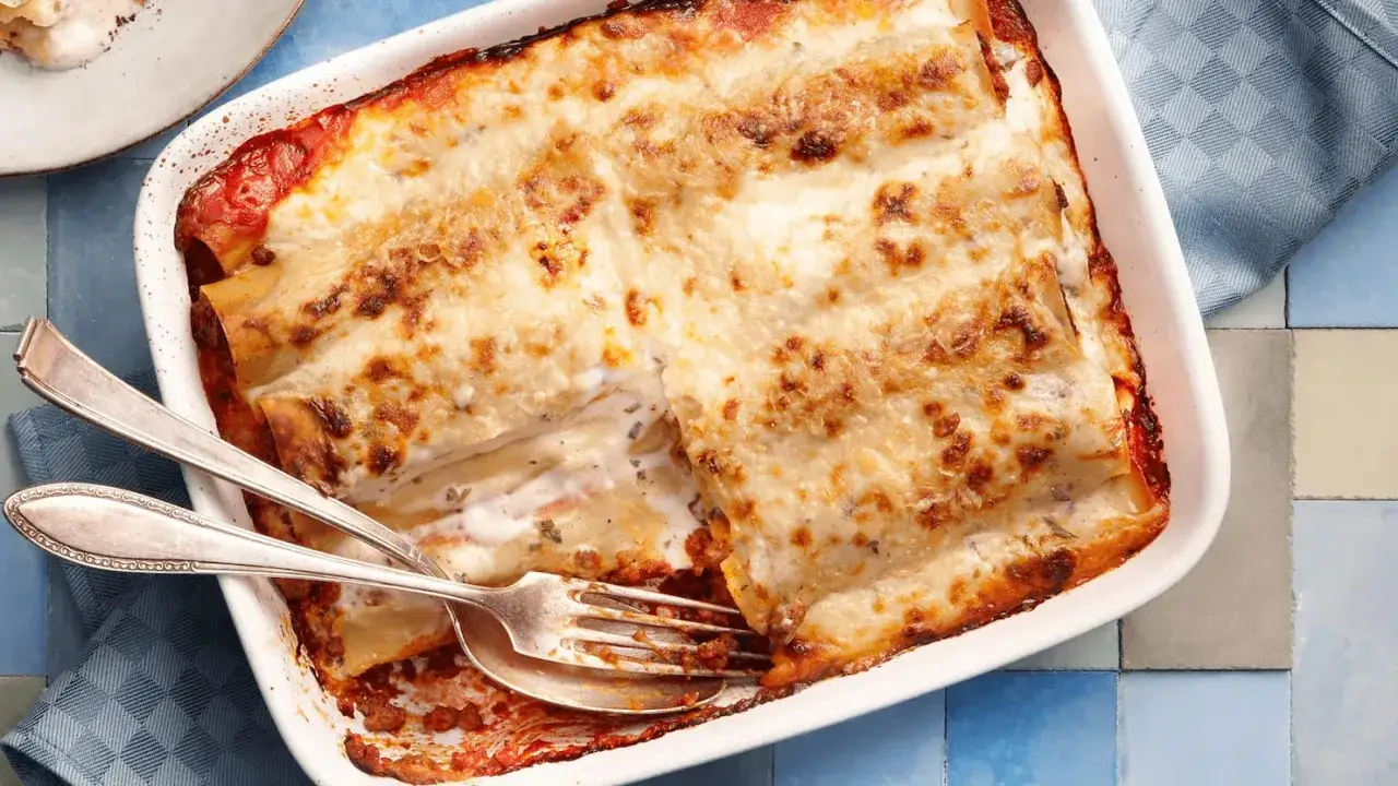 Herzhafte Cannelloni mit Hackfleisch, überbacken mit cremiger Käsesauce und goldbrauner Kruste. Ein Gabel und Löffel warten schon.