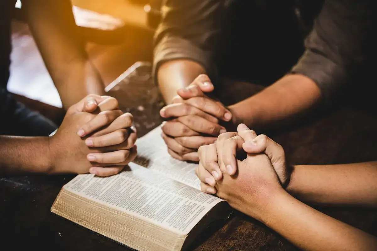 Hands clasped in prayer over an open Bible, a family shares a moment of devotion, offering prayers for children and guidance.