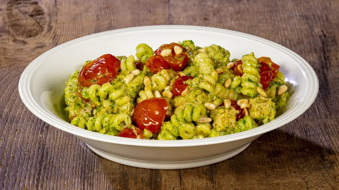 Un piatto invitante di pasta fredda al pesto, arricchita da tonno sfilacciato, pomodorini succosi e pinoli croccanti.