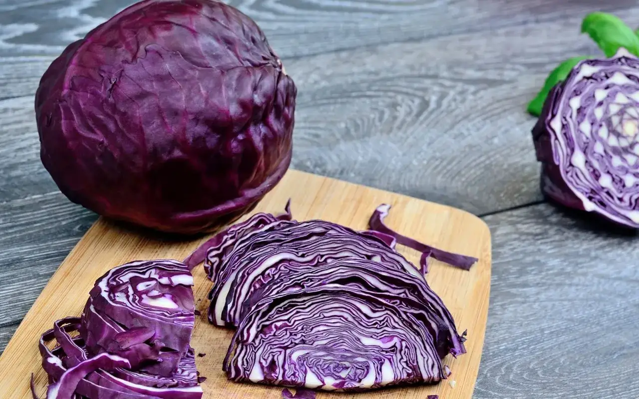 Cavolo cappuccio rosso intero e affettato su un tagliere di legno. Le fette mostrano le venature viola e bianche.