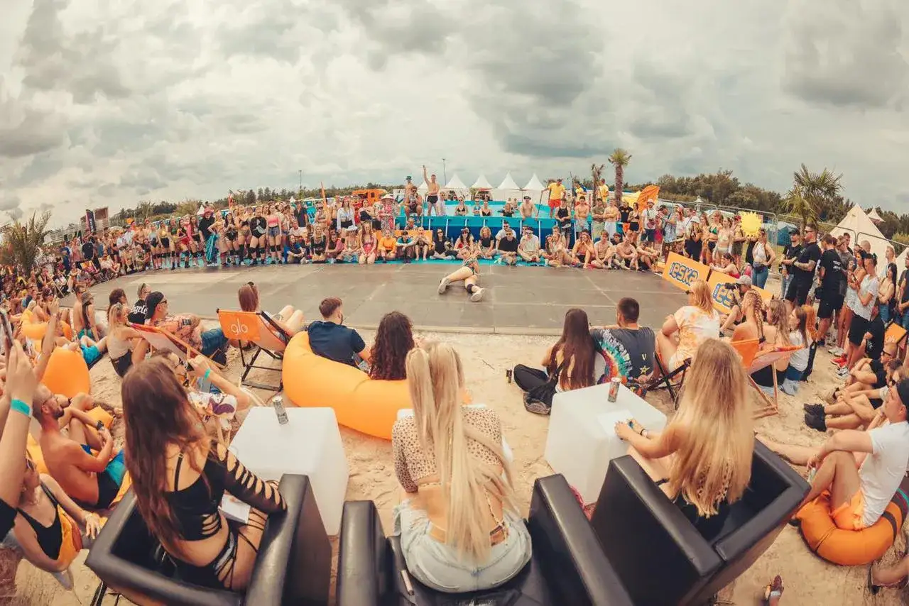 Tłum ludzi na plaży podczas festiwalu słońca, siedzą na kocach i leżakach, oglądając występ. W tle widać namioty i scenę.
