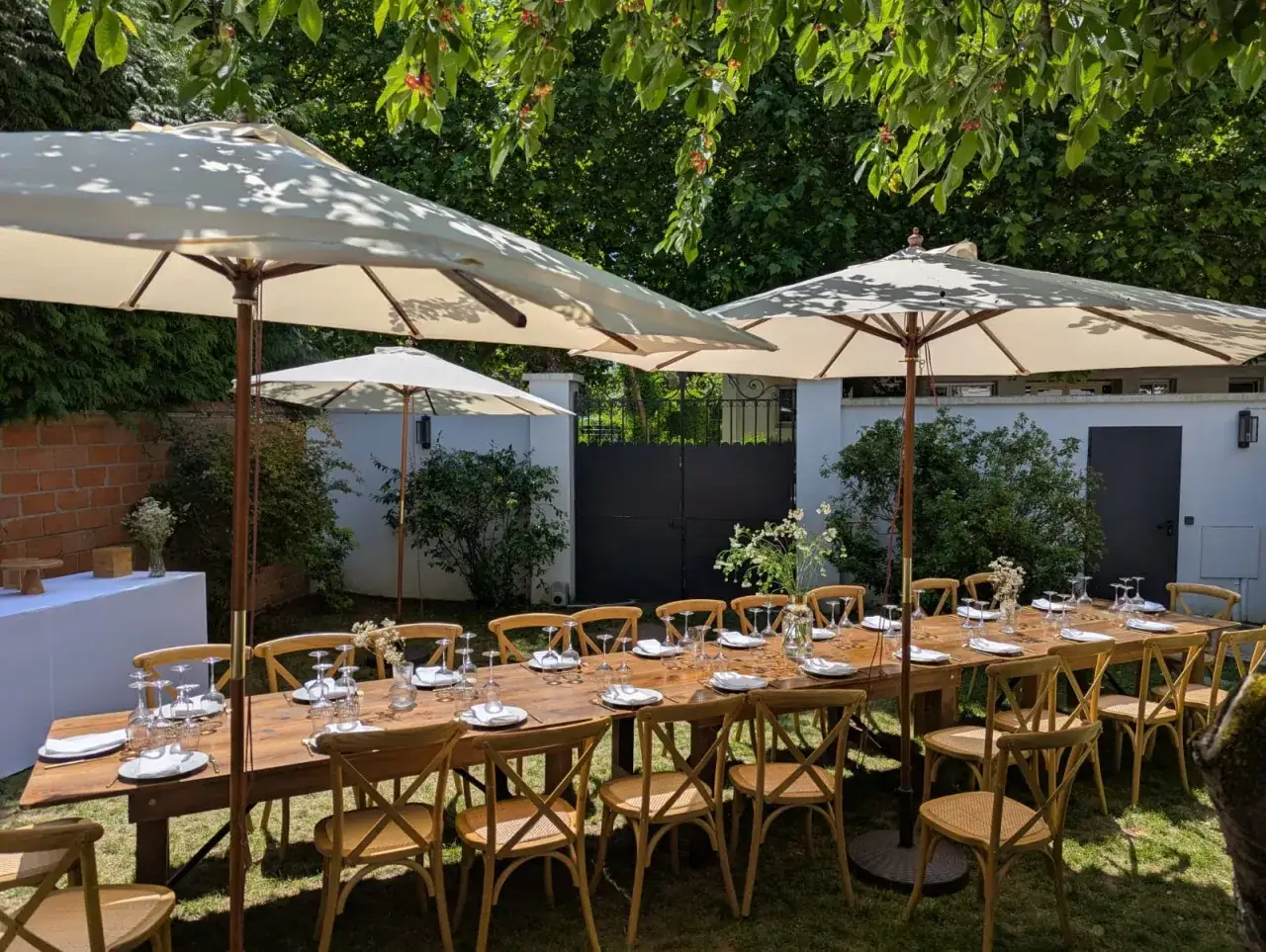 Table dressée pour un pique-nique chic sous les parasols, avec des chaises en bois et des verres étincelants.