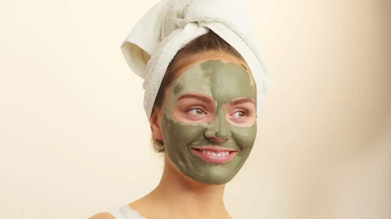 Mujer con toalla en la cabeza y mascarillas de arcilla para la cara, disfrutando de un momento de spa.