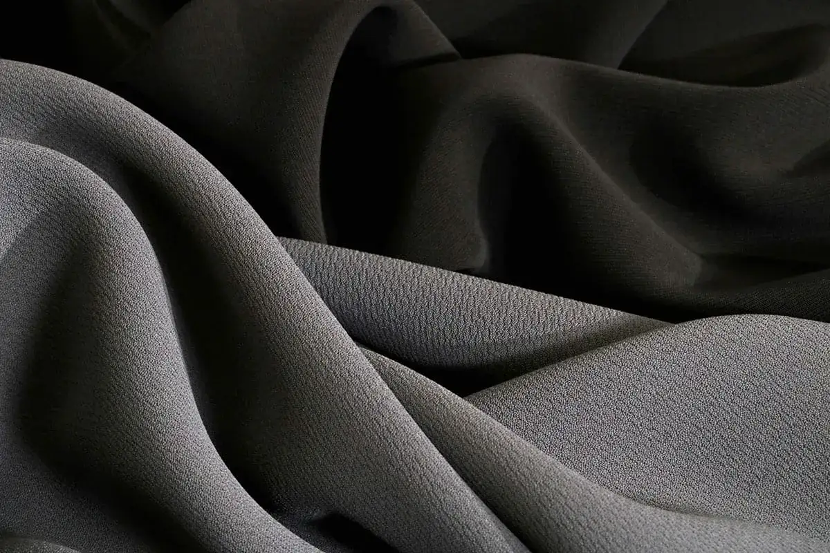 Drapierte Stoffe in Grau und Schwarz. Die Textur zeigt, was ist Polyester: ein vielseitiges Material, das sich gut falten lässt.