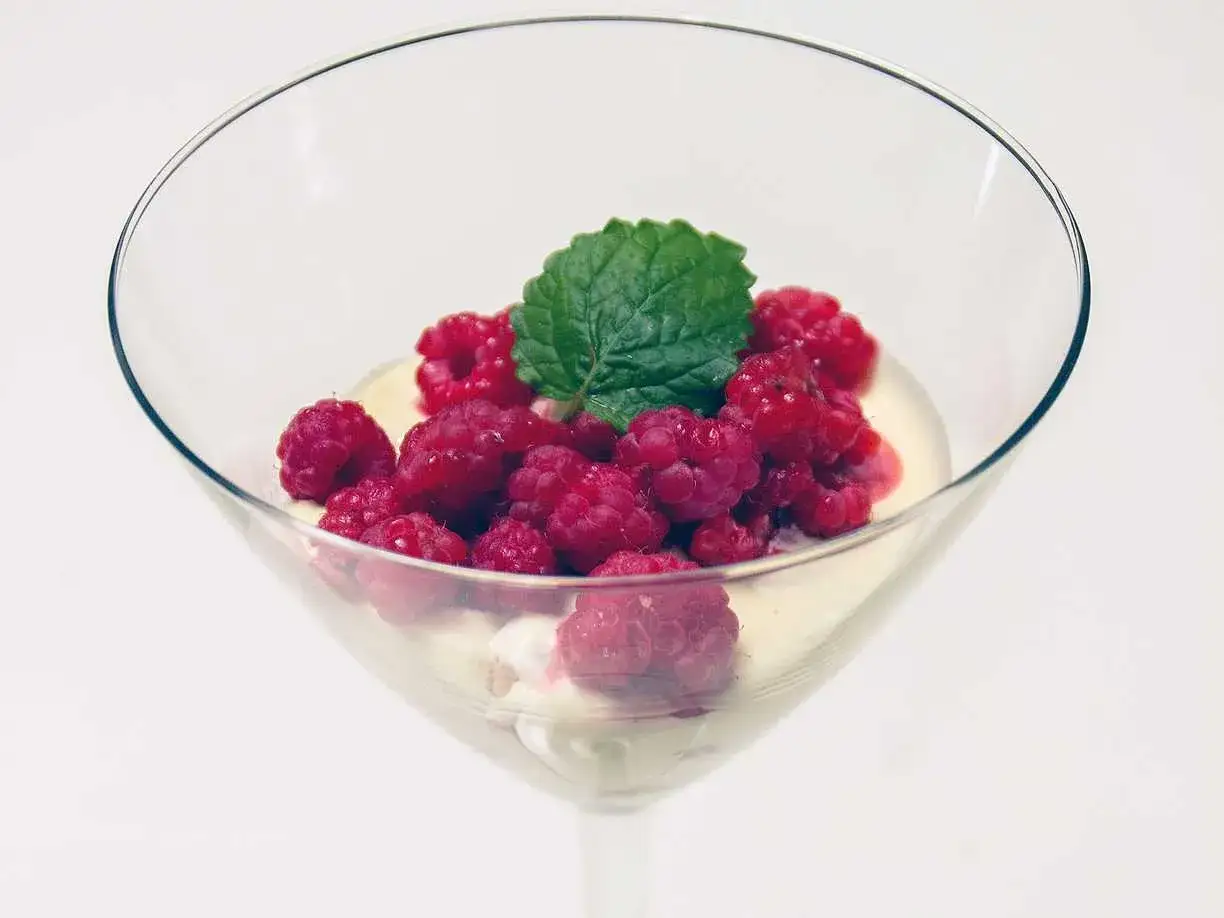 En elegant vit chokladmousse i ett glas, toppad med färska hallon och en myntakvist. En ljuvlig dessert.