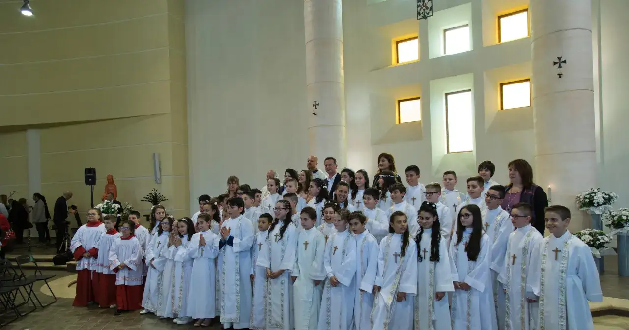 Dzieci w białych strojach komunijnych pozują do zdjęcia. Zastanawiasz się, ile trwa komunia? Zwykle uroczystość trwa około godziny.