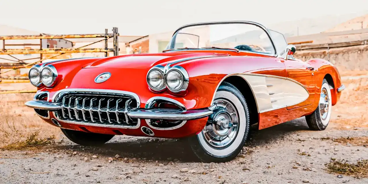 Czerwony muscle car Corvette z białymi wstawkami i chromowanymi detalami, stojący na żwirowej drodze.